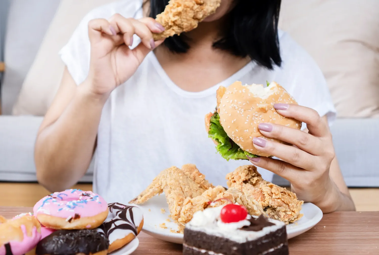 A woman seated at a table eating from a spread of fried food, burgers and desserts.